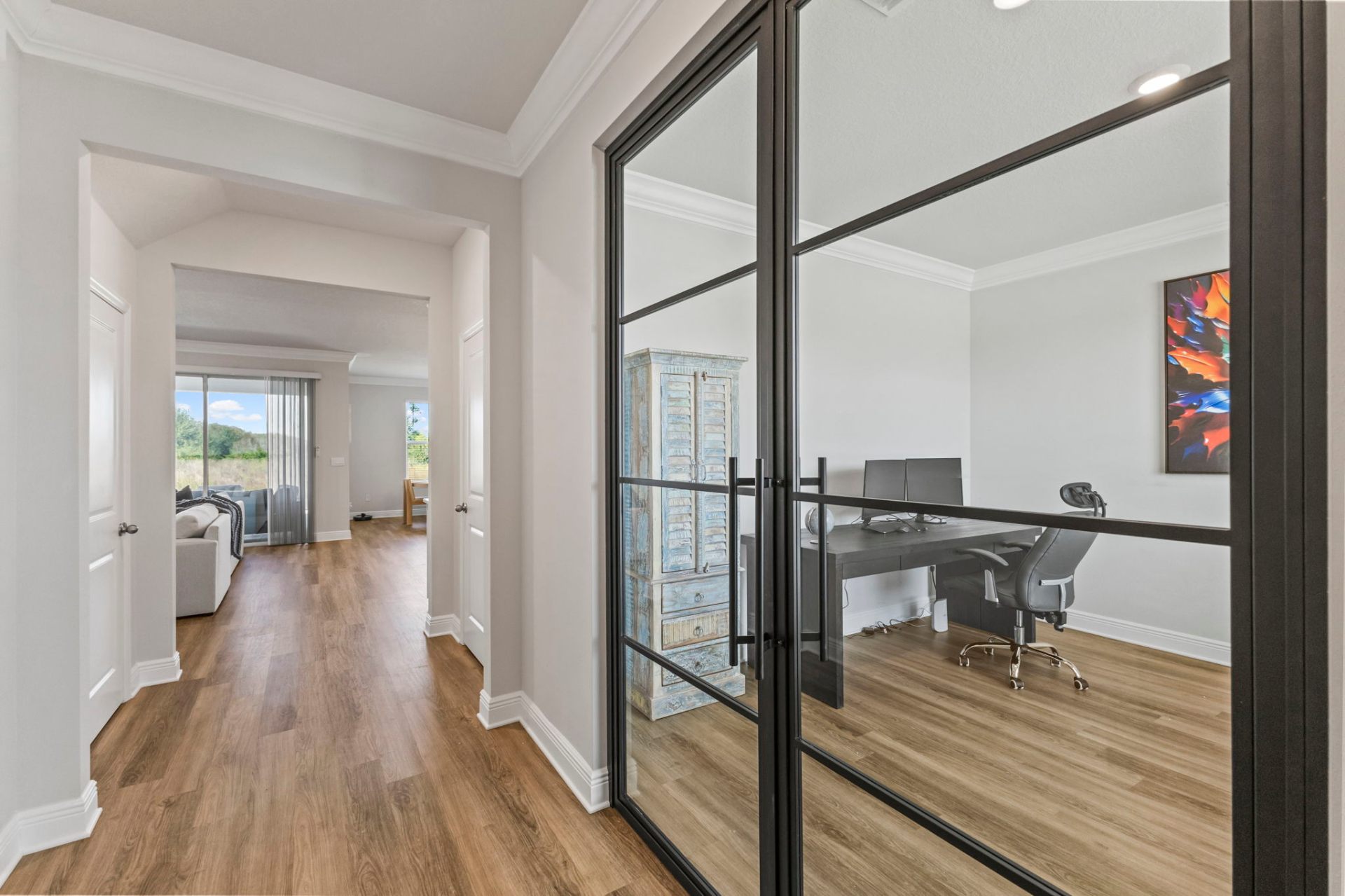 Hallway view into custom glass-enclosed home office with steel-frame doors