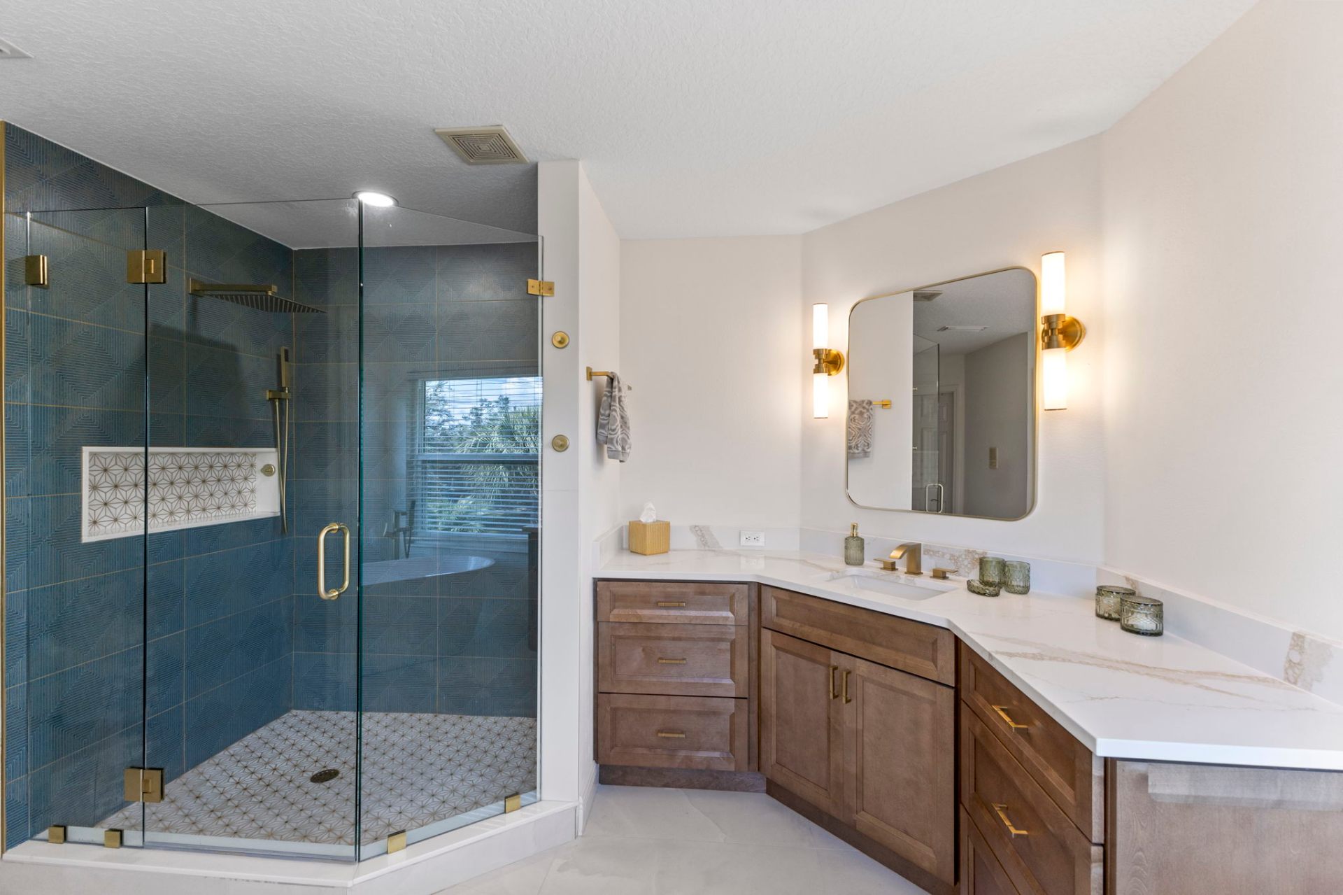 Primary bathroom with corner walk-in shower in blue tile and custom wood vanity with quartz top