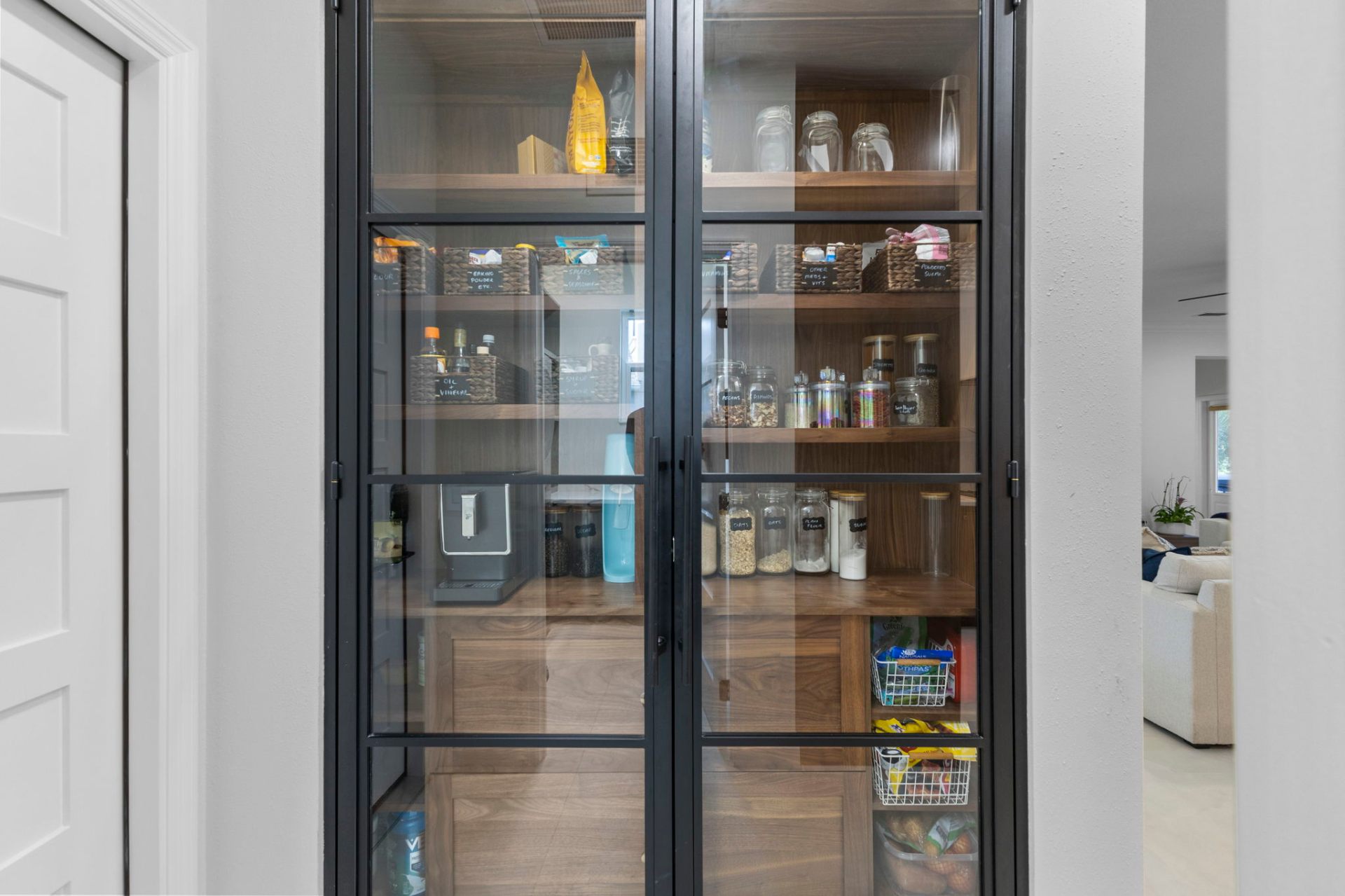 Custom walnut pantry behind black aluminum-framed glass doors with curated storage