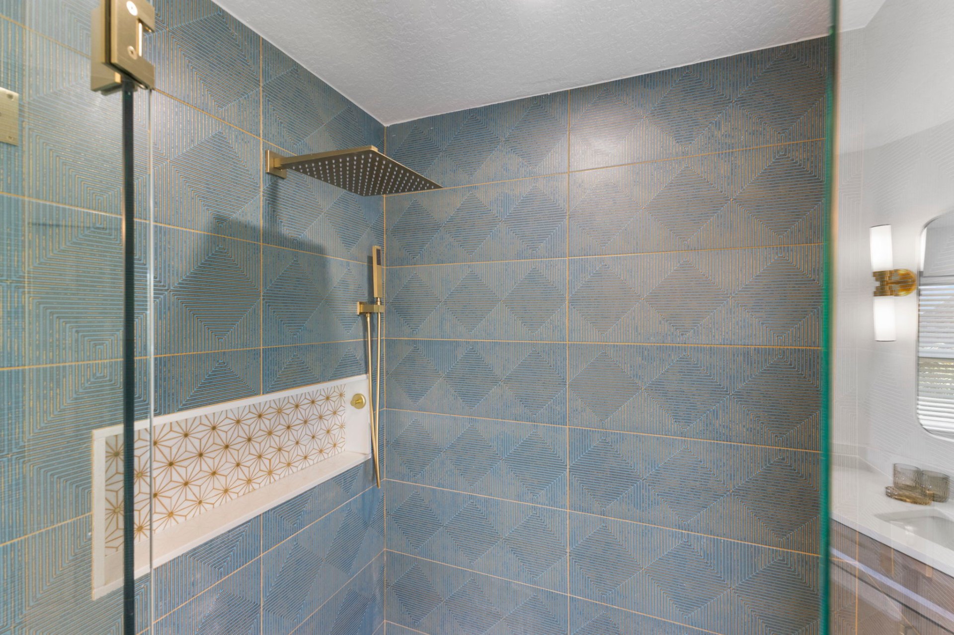 Walk-in shower with custom blue geometric tile, brass fixtures and starburst mosaic niche