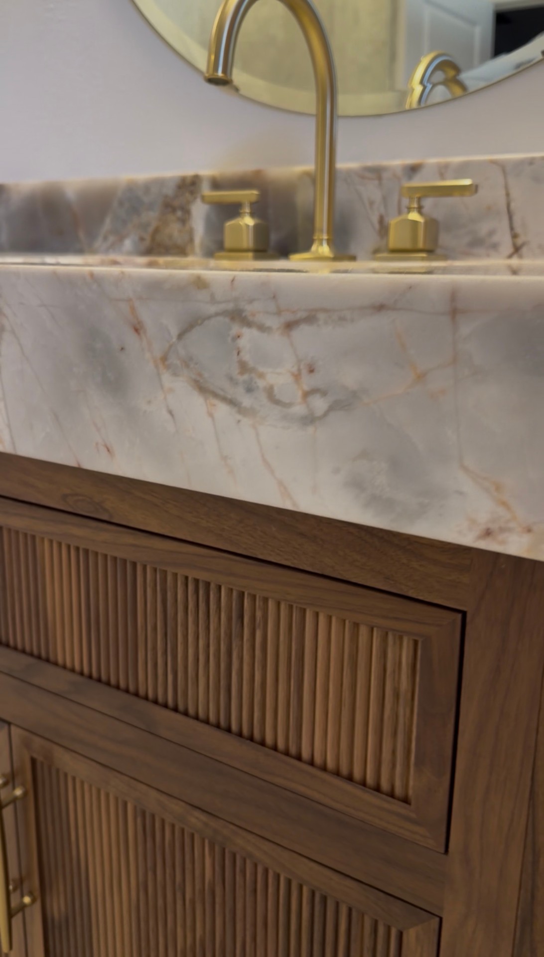 Detail of brushed brass widespread faucet on bookmatched quartzite countertop with custom walnut cabinetry
