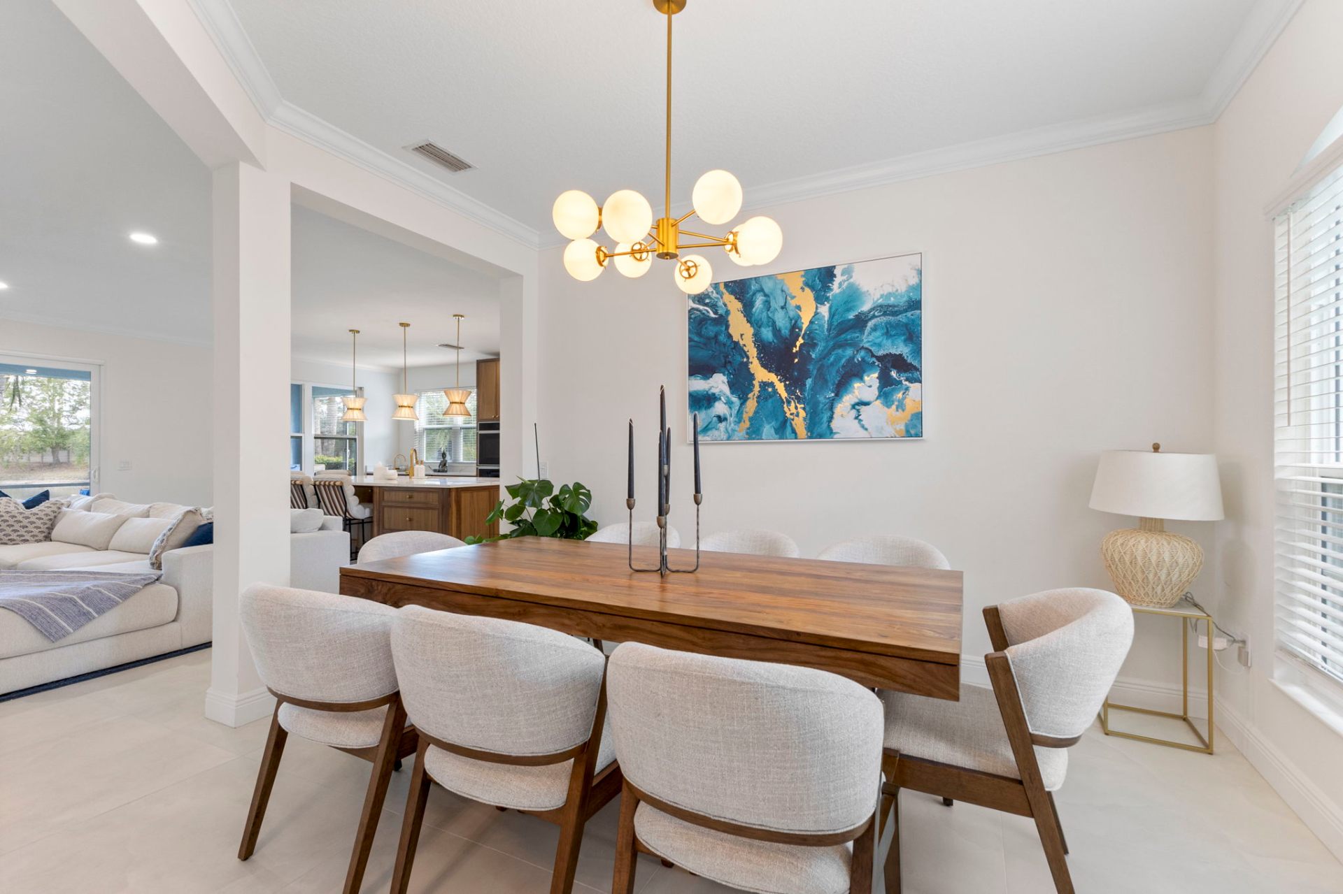 Dining room with custom artwork, brass chandelier and view through to the great room