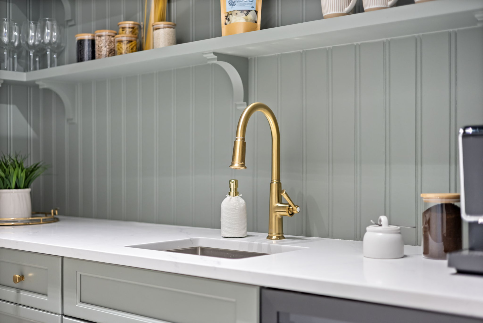 Detail of brass pull-down faucet against sage tongue-and-groove panelling