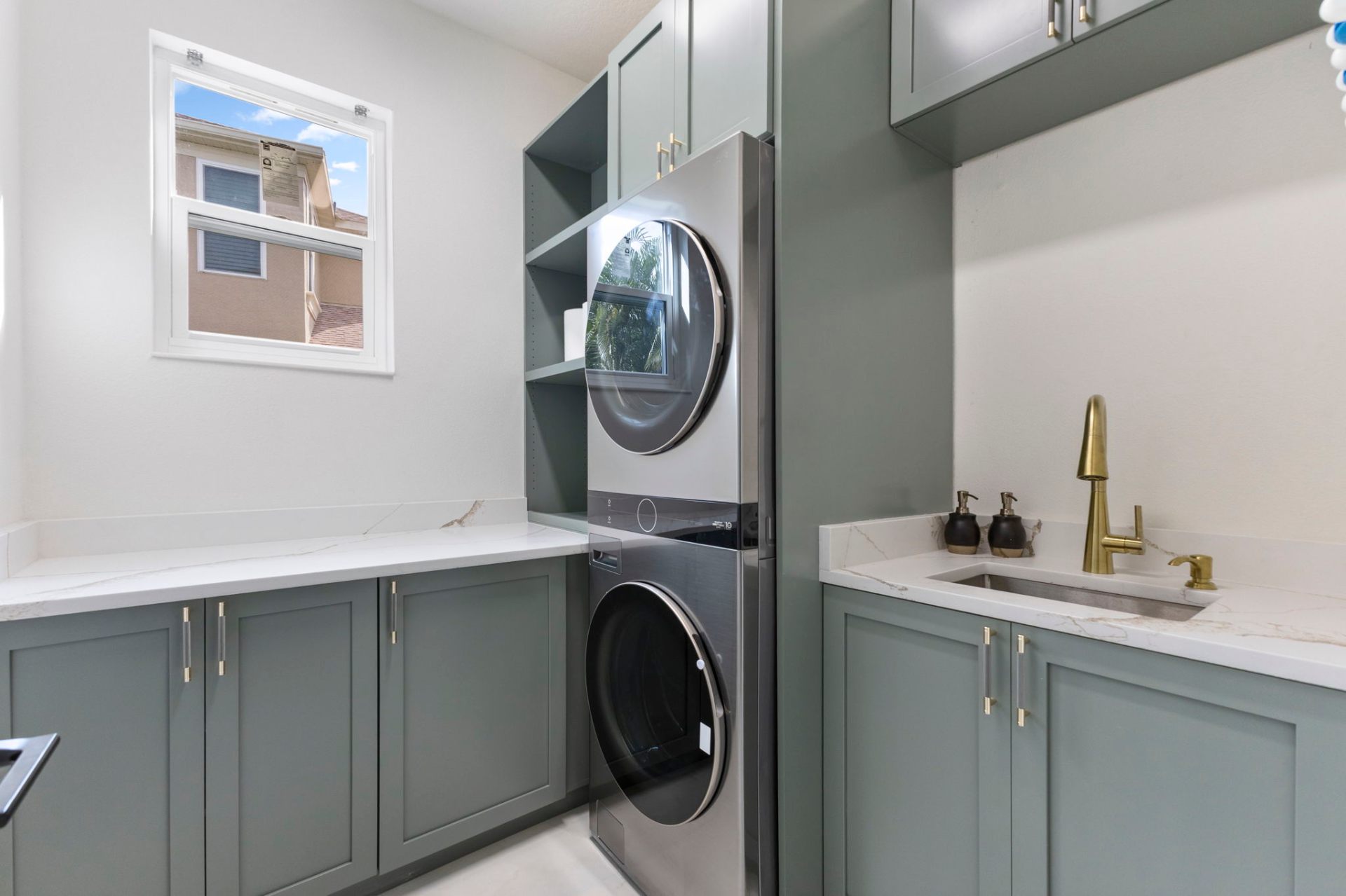 Custom laundry room with sage green shaker cabinetry, quartz counters and brass fixtures