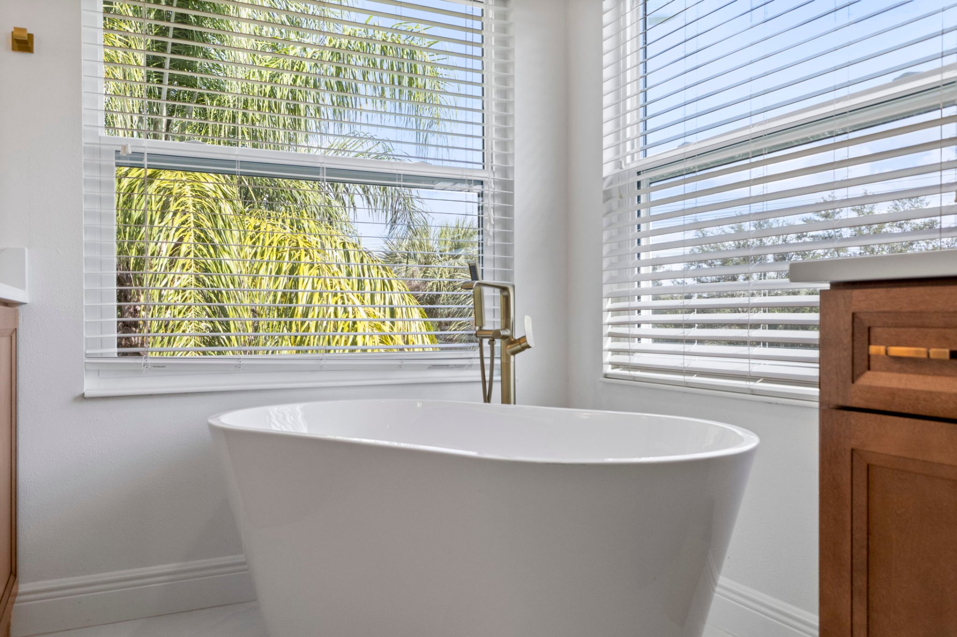Freestanding soaking tub framed by corner windows with palm garden views
