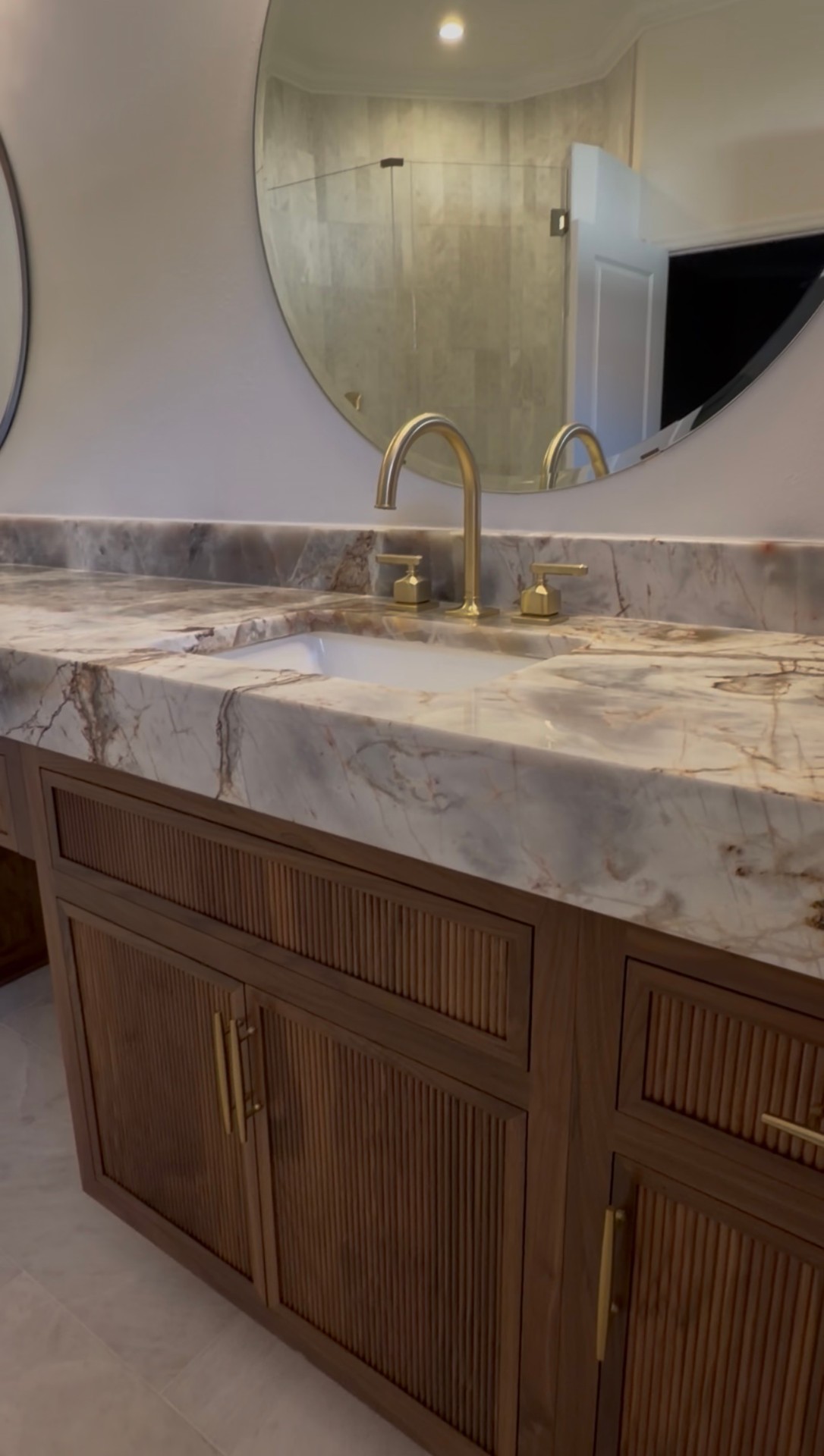 Dual walnut vanity with brass faucets, undermount sinks and round mirrors against quartzite backsplash