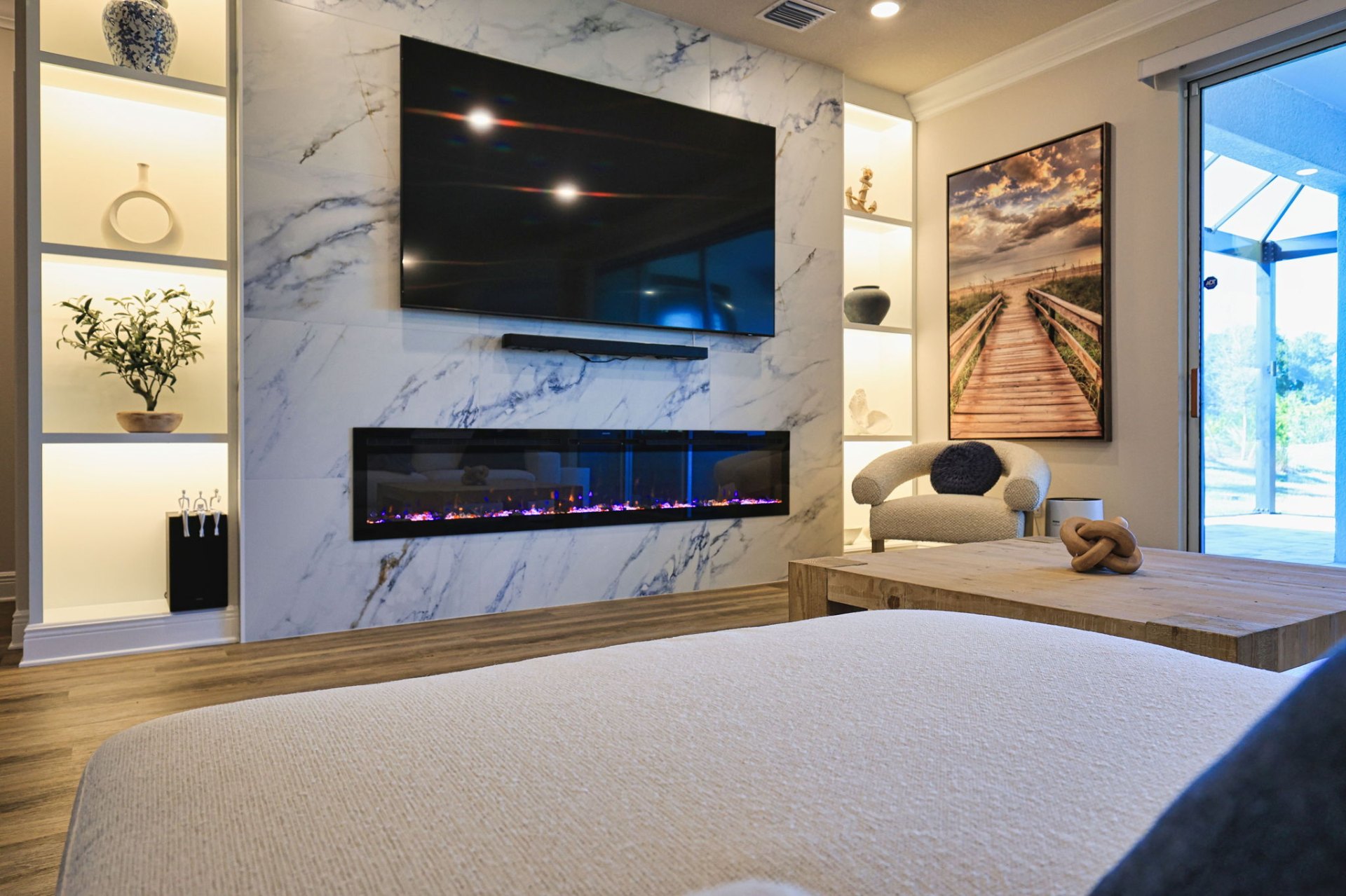 Primary bedroom with custom marble feature wall, mounted television and linear fireplace