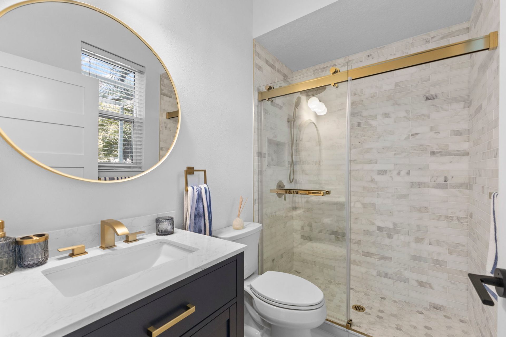 Renovated secondary bathroom with marble tile shower, navy vanity and brass hardware