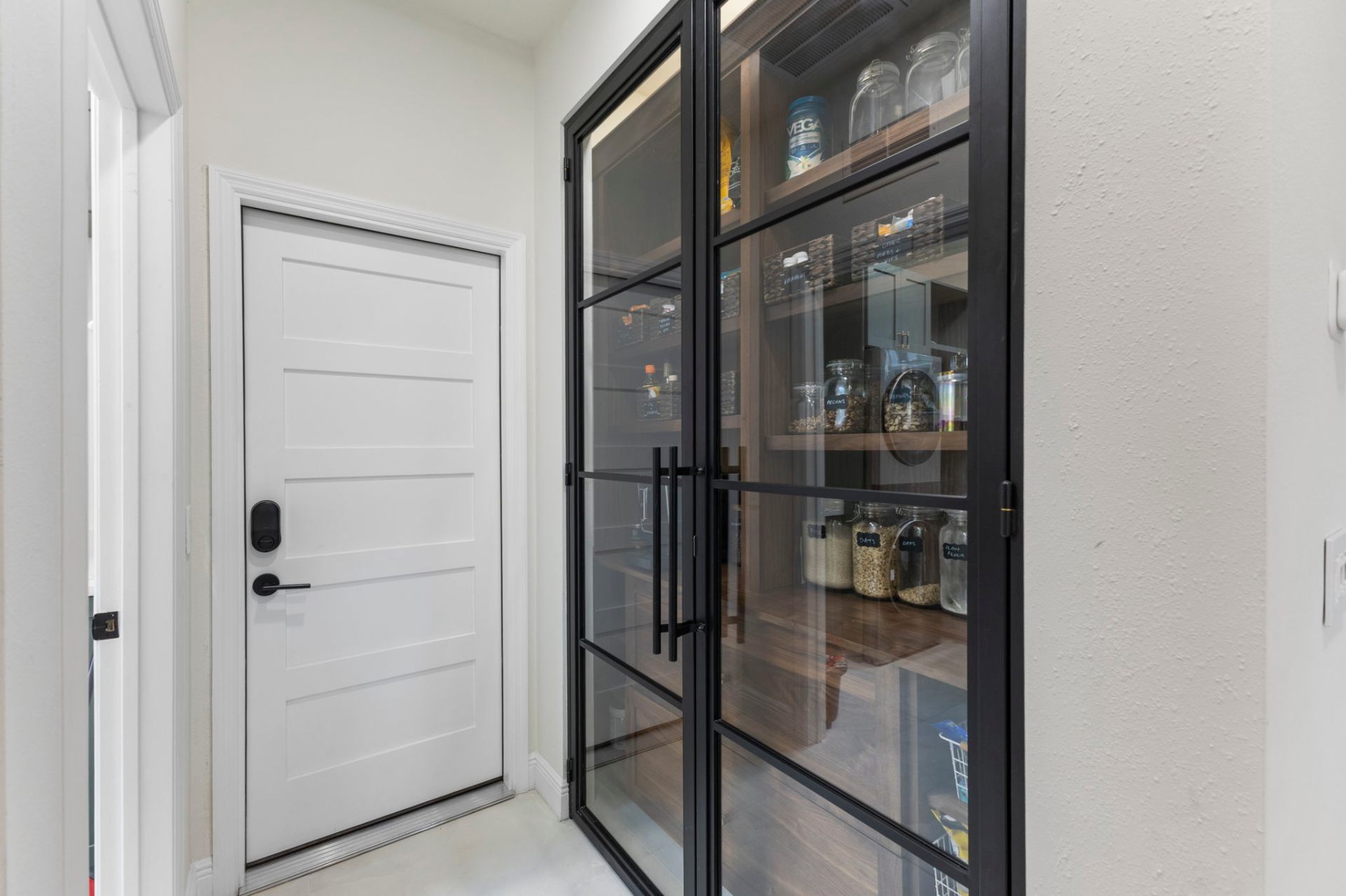Black aluminum-framed glass pantry doors set into the hallway with custom interior