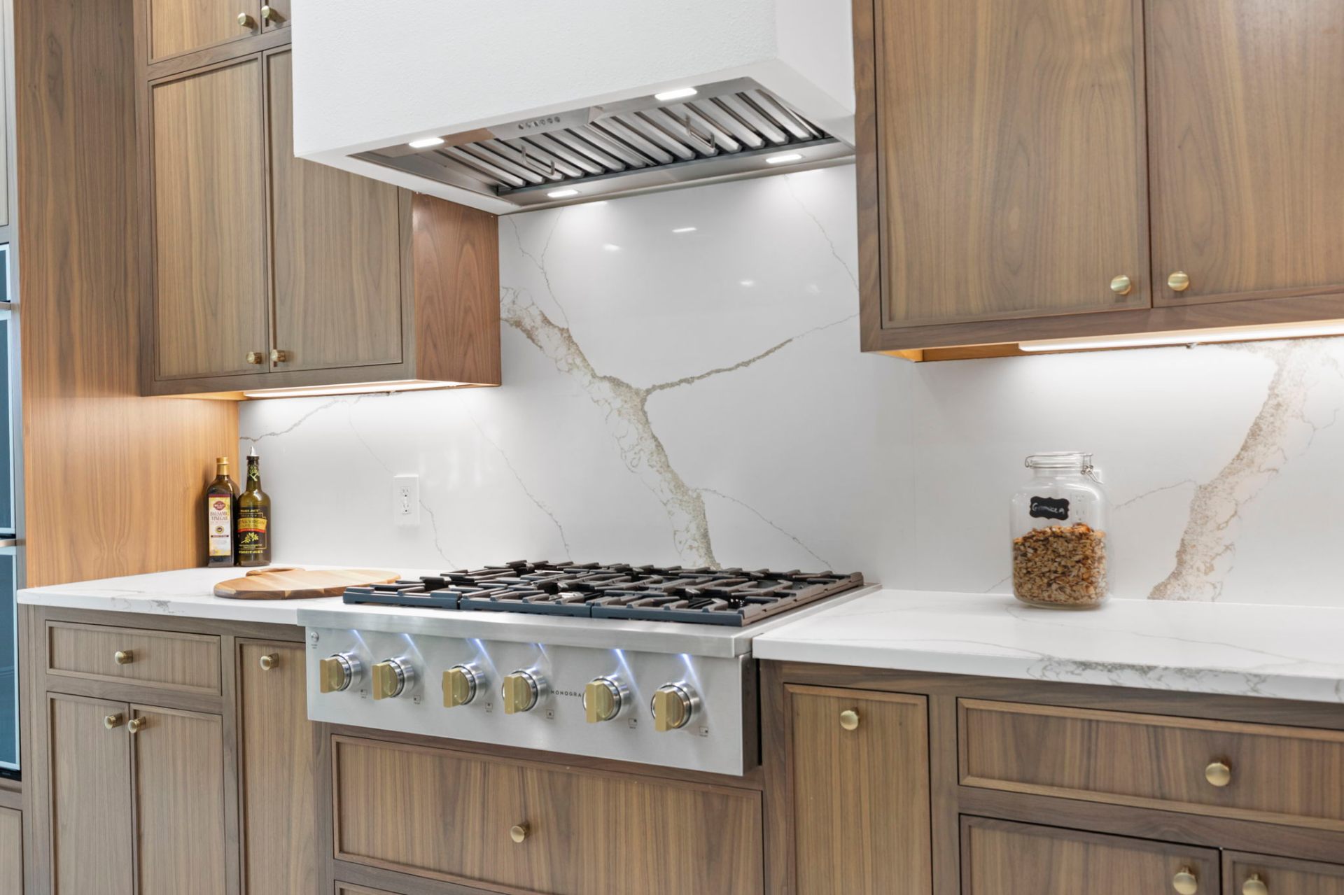 Detail of monogram gas cooktop, custom hood and bookmatched quartz backsplash